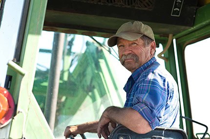 Farm equipment operator working on a green tractor in a rural setting.